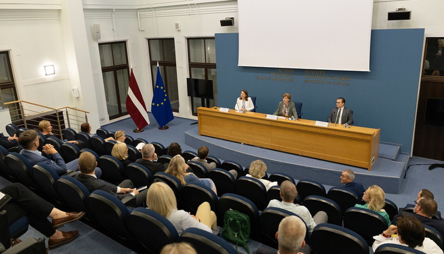 Ministre uzrunā pasākuma dalībniekus, kas sēž zālē